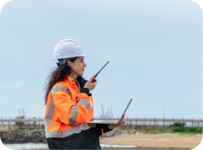A woman in an orange safety vest holds a laptop, representing Port-Side Management & Landside Integration efforts
