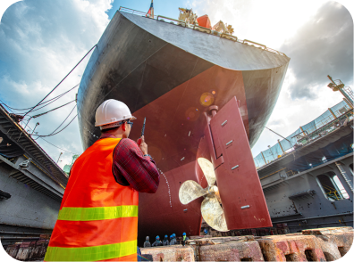 A man in an orange vest stands beside a large ship, part of the Marine Technical Support team during dockside operations